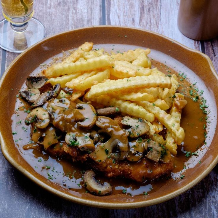 a plate topped with meat covered in gravy next to french fries and mushrooms