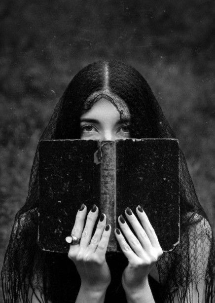 a woman with long hair covering her face and holding an old book in front of her face