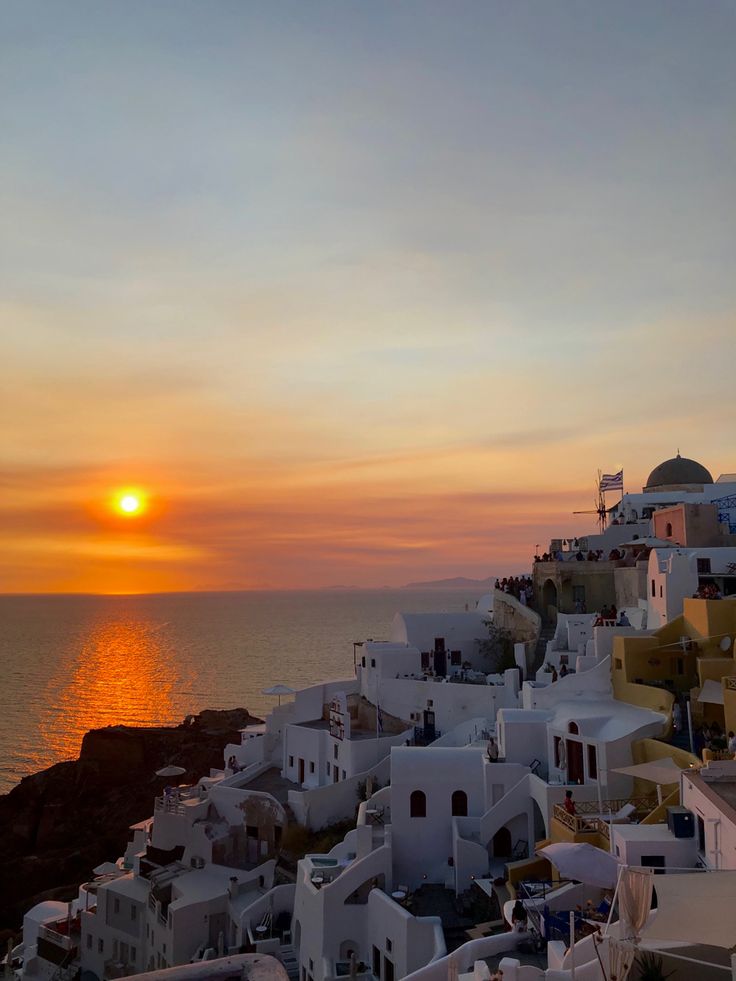 the sun is setting over some white buildings by the ocean in oia, greece