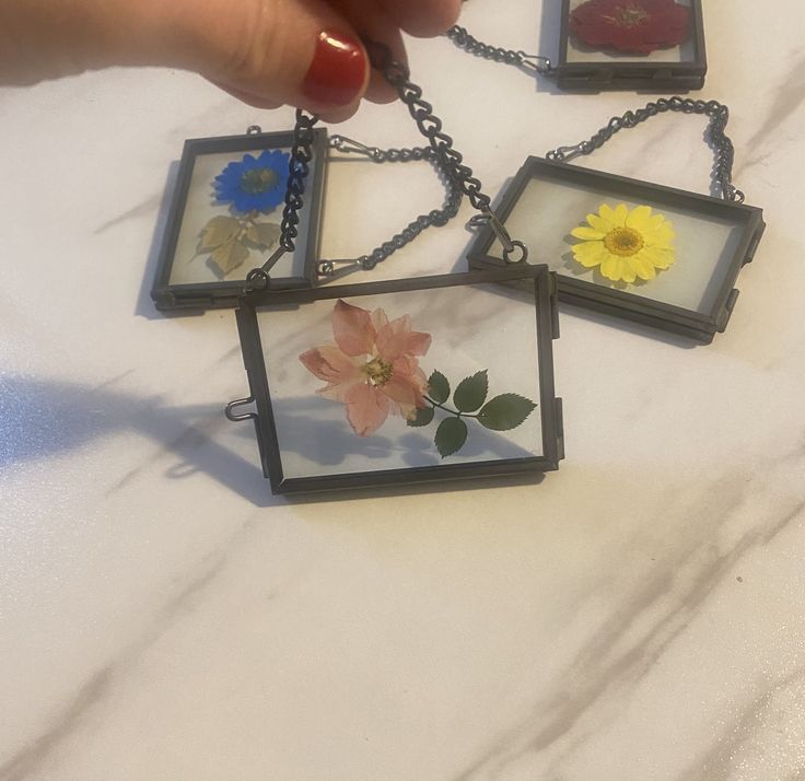 a person is holding four small square pendants with flowers in them on a table