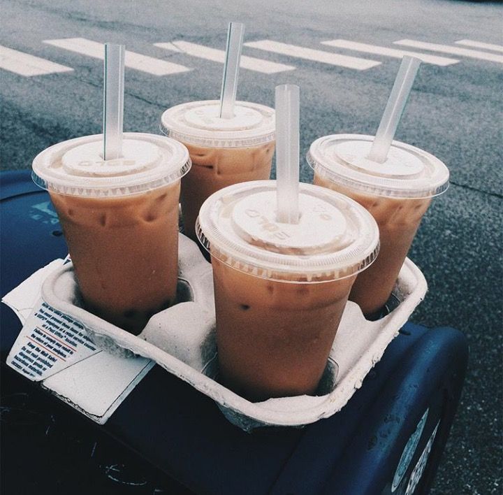 four iced coffees are sitting in a carton on the side of the road