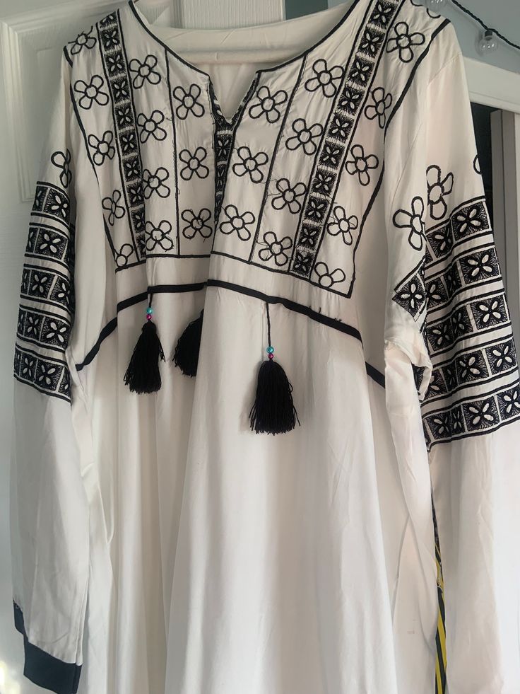 Embroidered long sleeve kuftan cool white material with black flower design embroidery Traditional White Kaftan With Tassels, Traditional Spring Kaftan With Tassels, Casual White Long Sleeve Kaftan, Long Sleeve Kaftan With Tassels For Spring, Long Sleeve Spring Kaftan With Tassels, White Long Sleeve Blouse With Embroidered Sleeves, Spring Long Sleeve Embroidered Kaftan, Traditional Long Sleeve Kaftan With Tassels, White Long Sleeve Blouse With Embroidered Hem