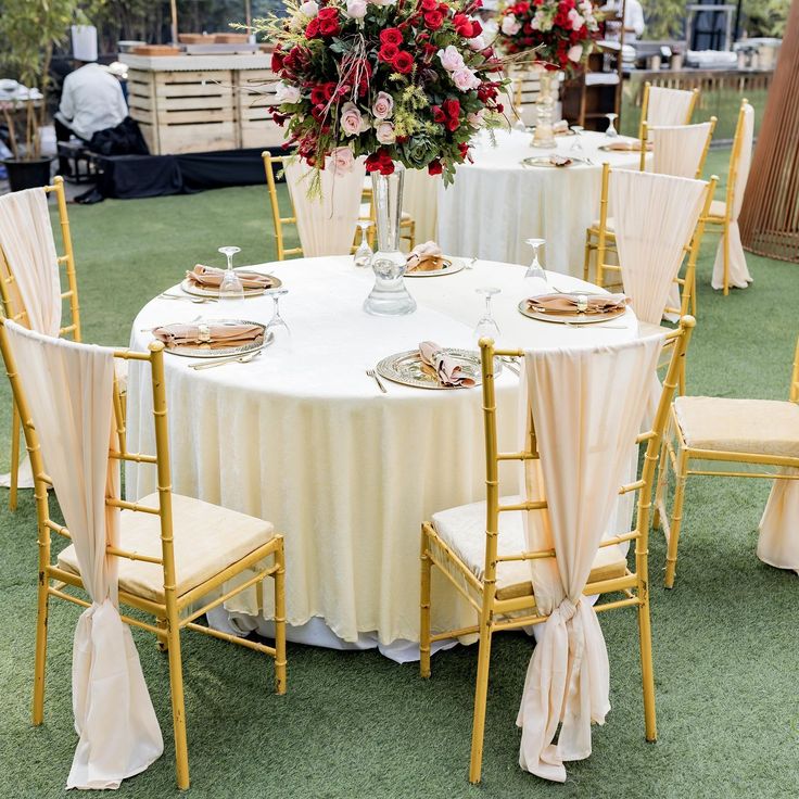 the table is set with white linens, gold chairs and red flowers in vases