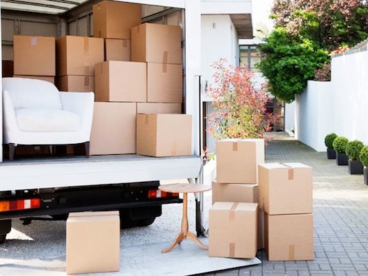 a white couch sitting in the back of a moving truck with cardboard boxes on it