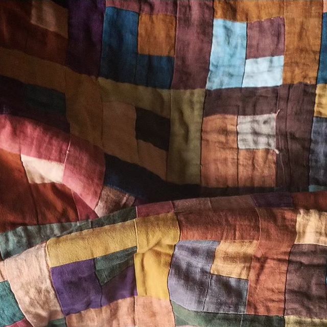 an old quilt is laying on top of a tablecloth covered in multicolored squares