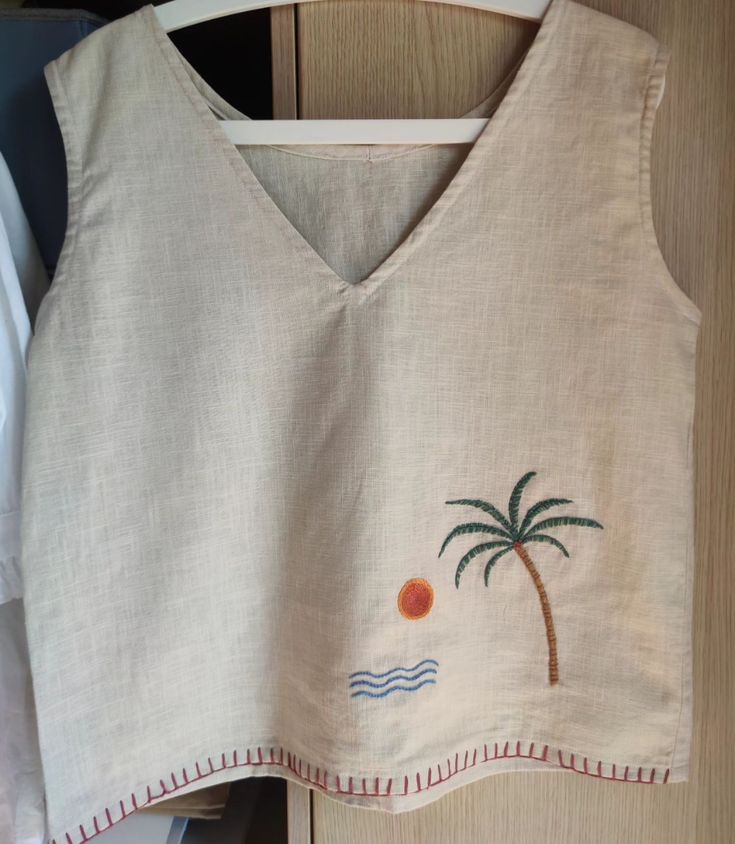 an embroidered top with a palm tree on the front and beach scene on the back