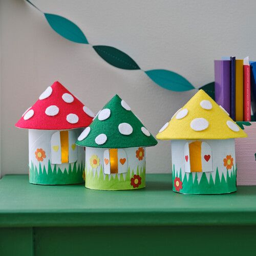 three little houses made out of toilet paper on a green table next to bookshelves