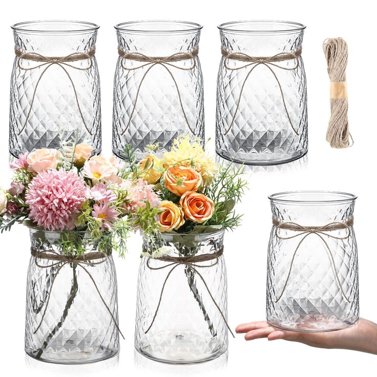 four glass vases with flowers in them and one being held by someone's hand