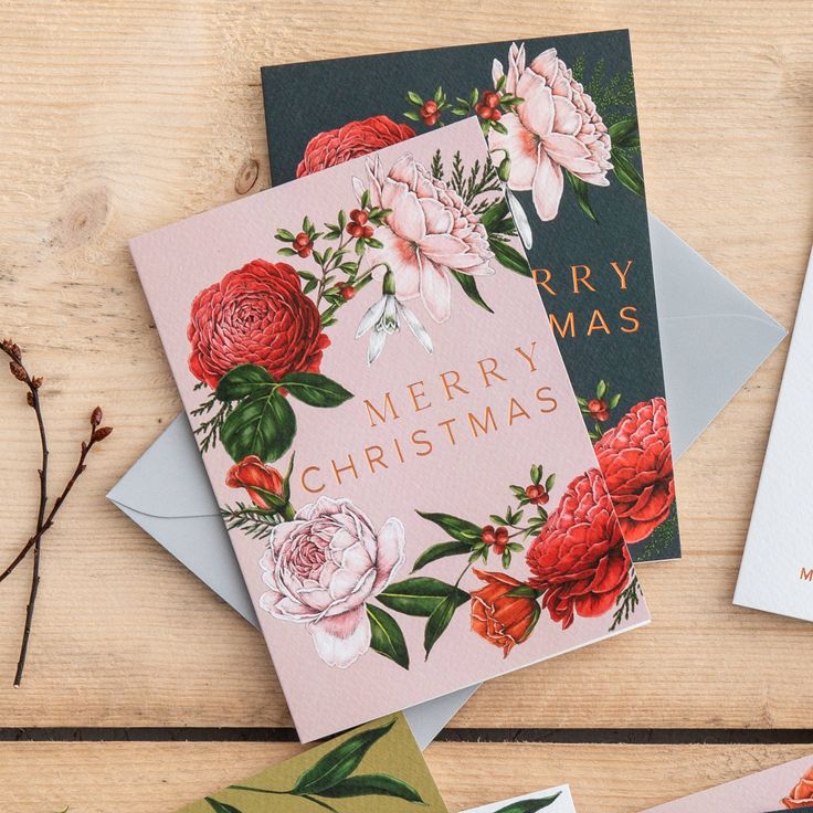 three christmas cards sitting on top of each other next to envelopes with flowers and the words merry christmas