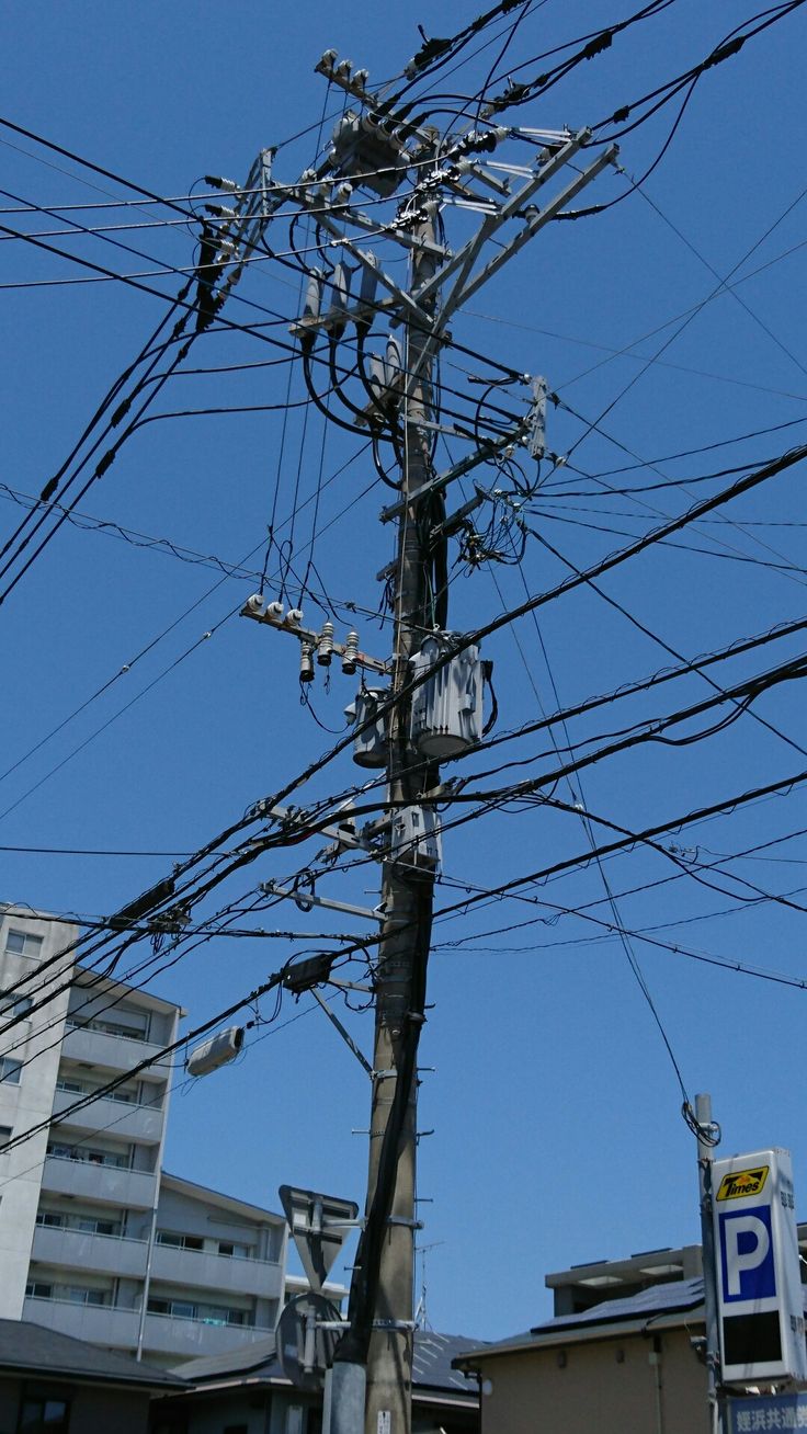 an electric pole with lots of wires above it and buildings in the background on a sunny day