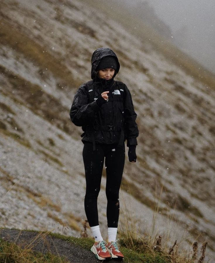 a woman standing on the side of a snow covered mountain with her hands in her pockets