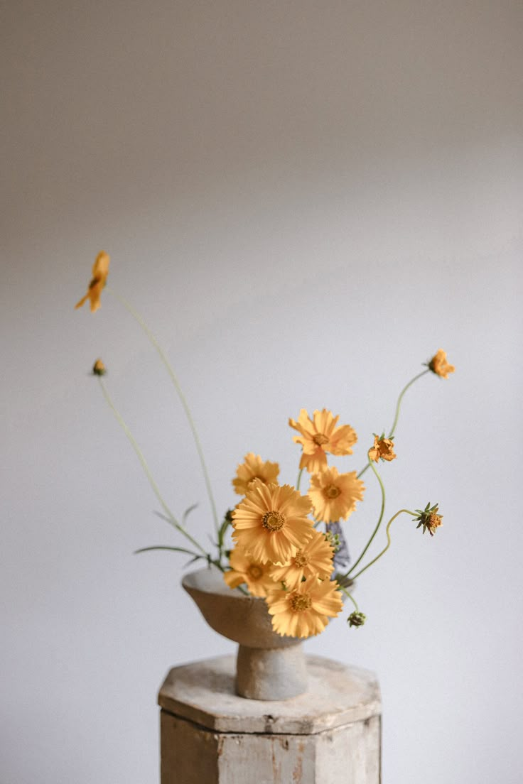 some yellow flowers are in a vase on top of a white box and it is sitting on a table