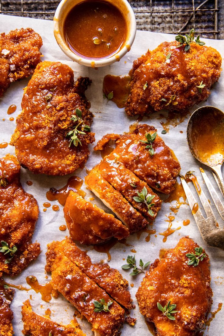 fried chicken with sauce and herbs on a sheet of parchment paper next to a fork