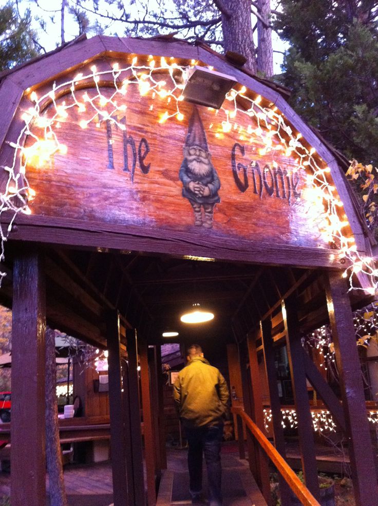 a man walking down a wooden walkway under a lit up sign that says the gnome