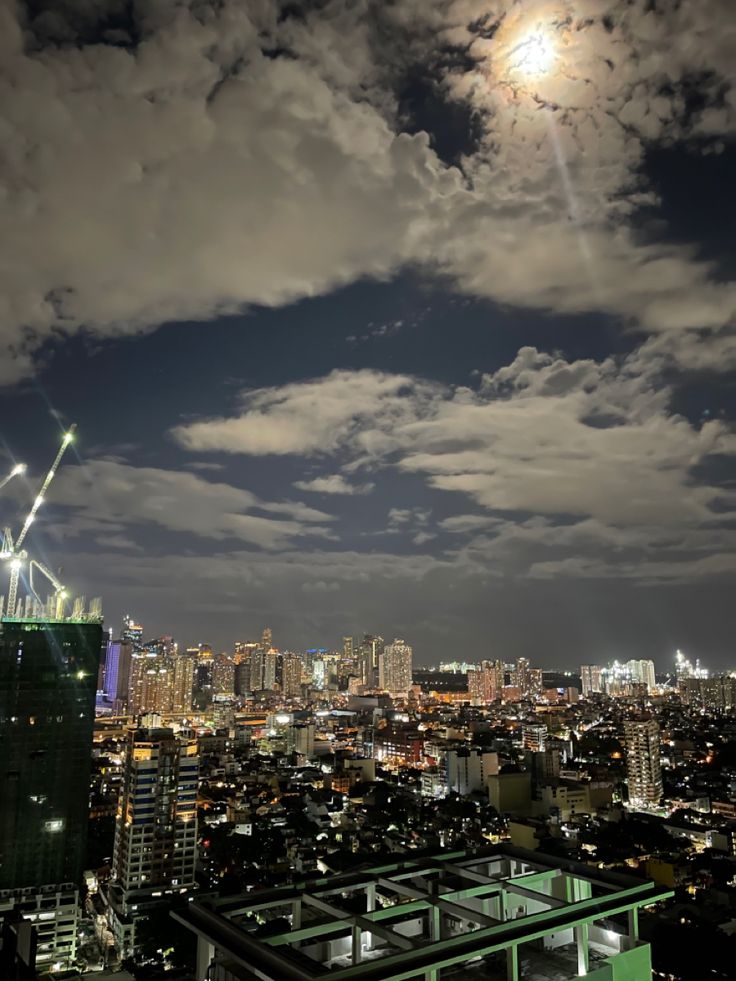 the city skyline is lit up at night with bright lights and clouds in the sky