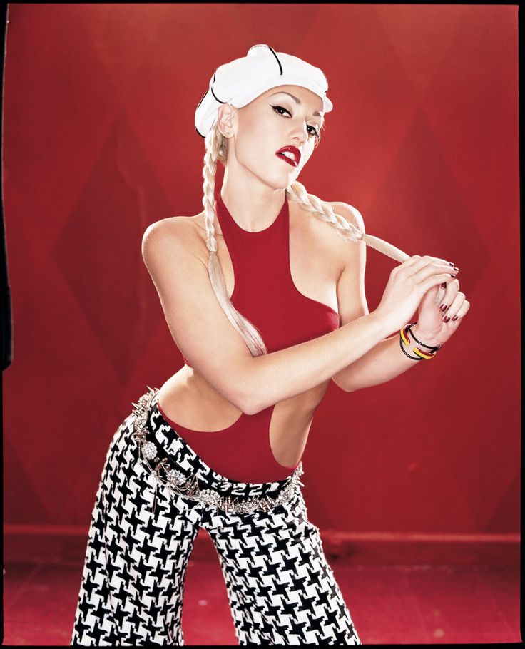 a woman in red top and patterned pants holding a baseball bat with both hands on her hip