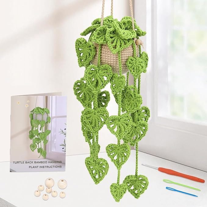 a green crocheted plant hanging from a window sill next to a book