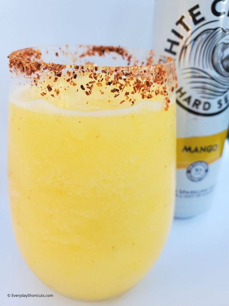 a yellow drink in a glass next to a bottle of alcohol and some spices on the rim