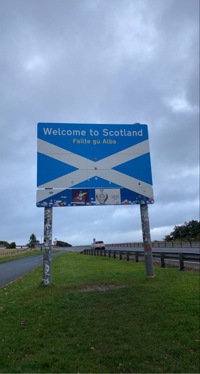 a blue and white sign sitting on the side of a road next to a lush green field