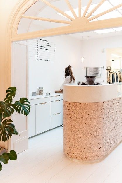 a woman is standing at the counter in front of a white wall and plants on the floor