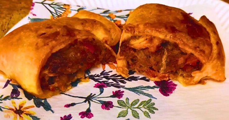 two pieces of meat filled pastries on a paper plate