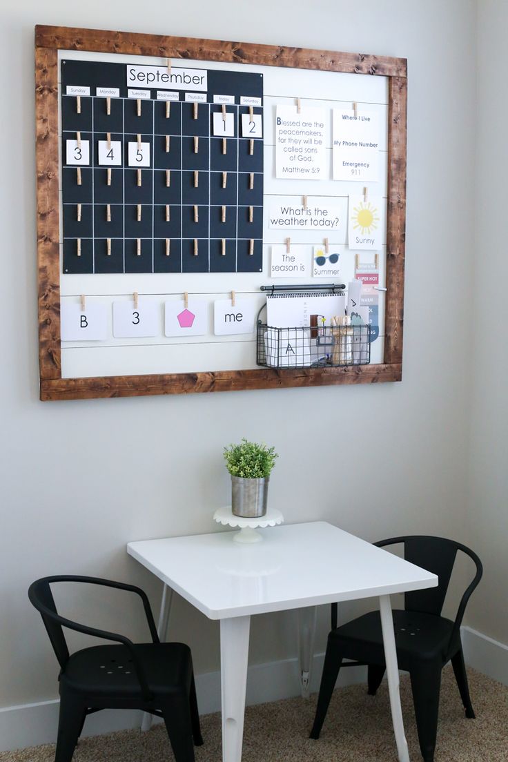 a white table and two black chairs in front of a calendar on the wall above it