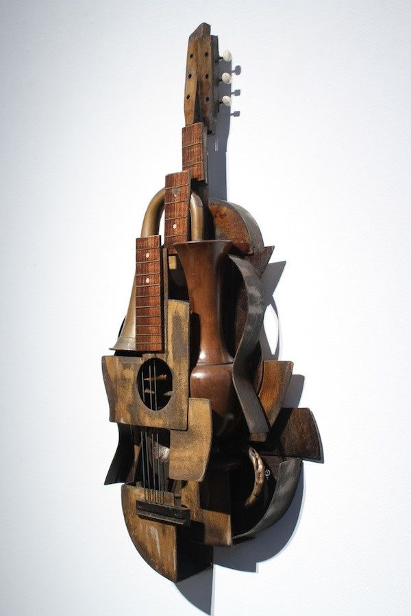 a guitar sculpture hanging on the wall in front of a white wall with no one around it