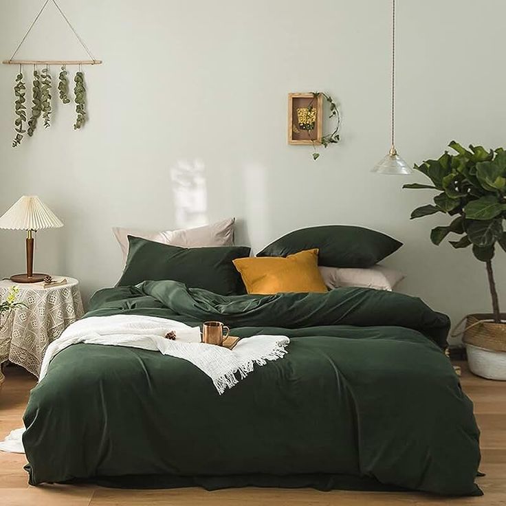 a bed with green sheets and pillows in a room next to a potted plant