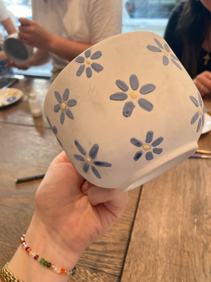 a person holding up a blue and white hat on top of a wooden table with other people in the background