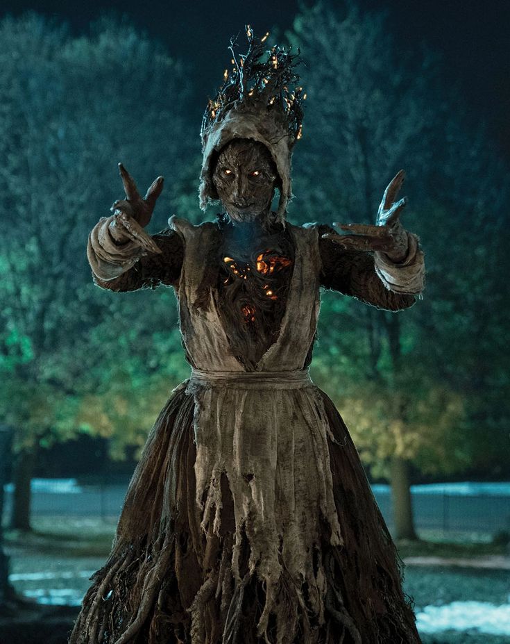 a woman dressed as a scarecrow standing in the dark with her hands up and wearing a crown