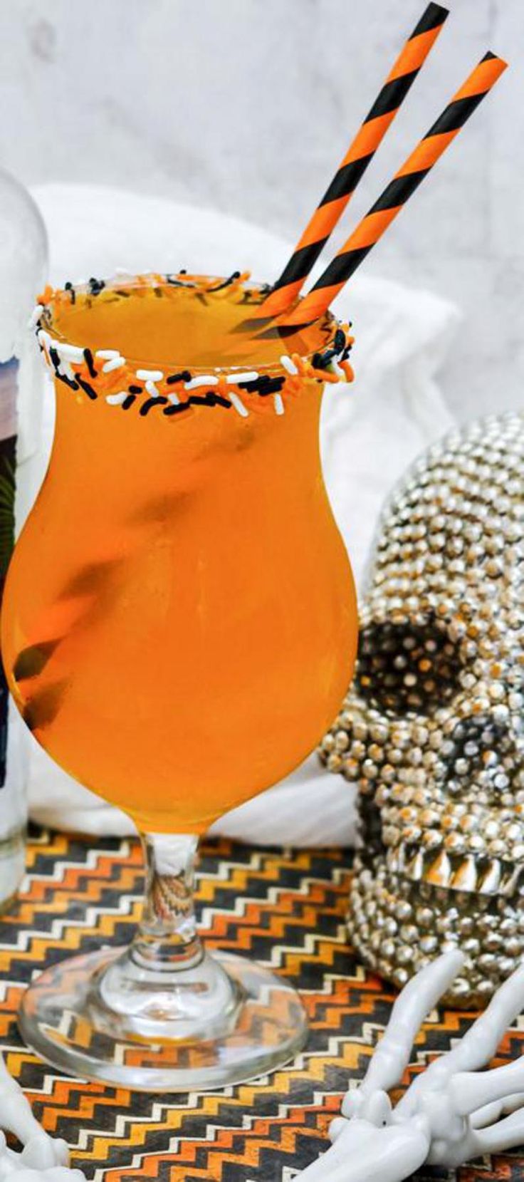 an orange drink with black and white straws in a glass next to halloween decorations