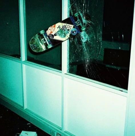 a skateboarder is about to fall off his board in the air over a broken window