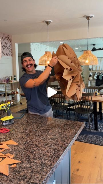 a man standing in front of a kitchen counter holding up a piece of paper that has been cut into shapes