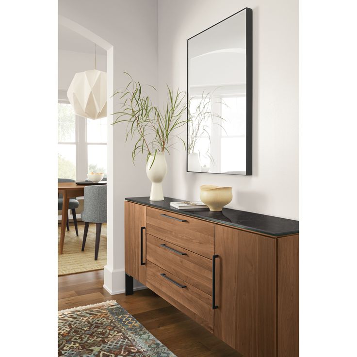 a large mirror hanging over a wooden dresser next to a vase with a plant on it