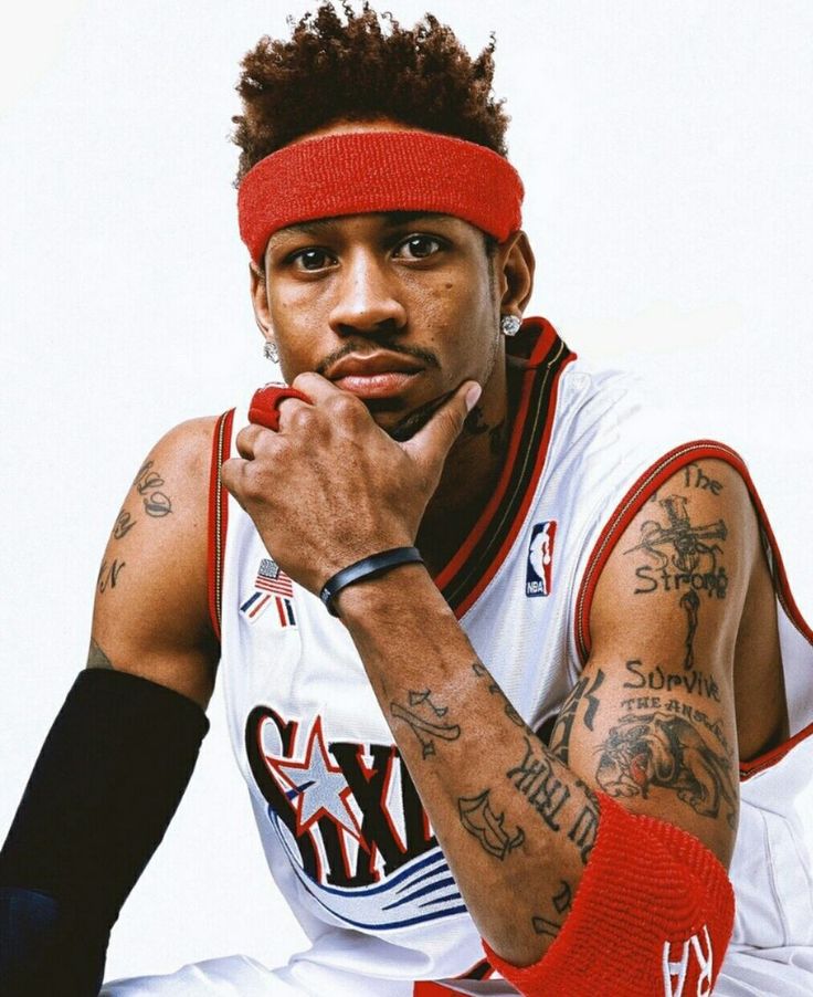 a man with tattoos sitting down wearing a red headband and looking at the camera