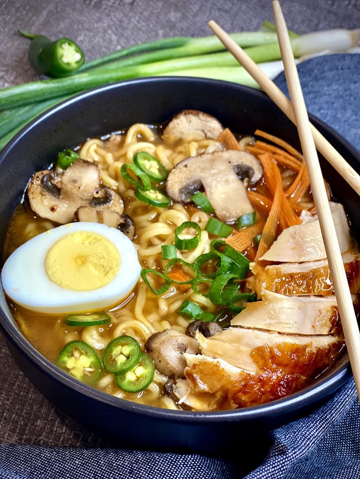 a bowl filled with noodles, meat and vegetables next to chopsticks on a table