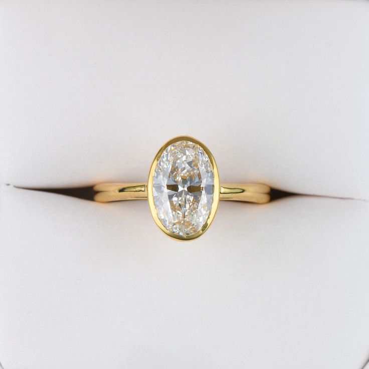 a yellow gold ring with an oval cut diamond in the center on a white background