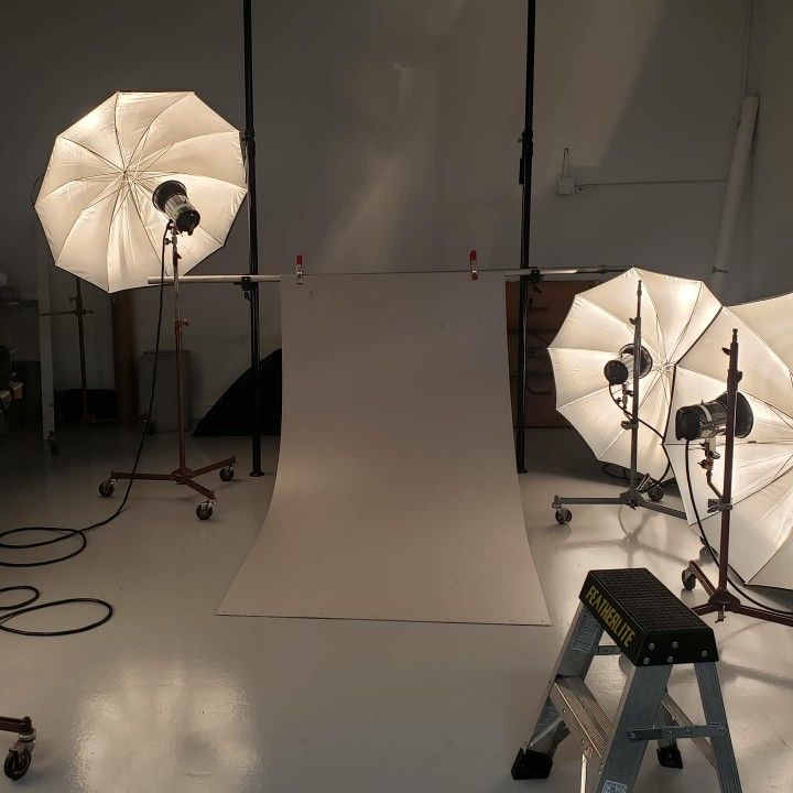 three umbrellas are set up in a studio with lights on the floor and behind them