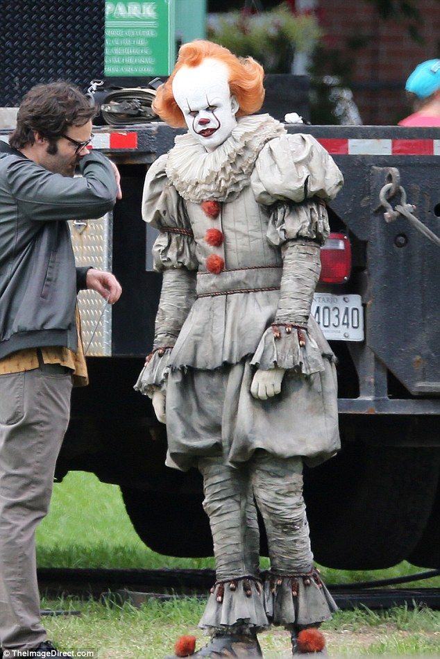 a man standing next to a creepy clown on top of a green grass covered field