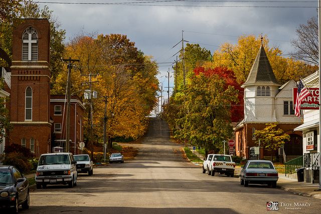 cars are parked on the street in front of buildings and trees with autumn foliage around them