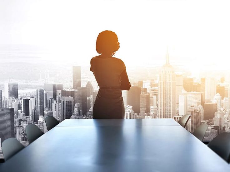 a woman standing at a conference table in front of a cityscape with skyscrapers