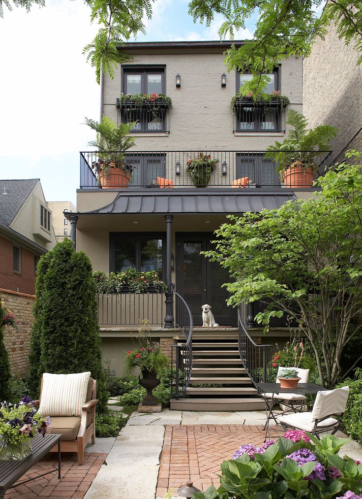 an outdoor patio with chairs and potted plants in front of a house that has stairs leading up to the second floor