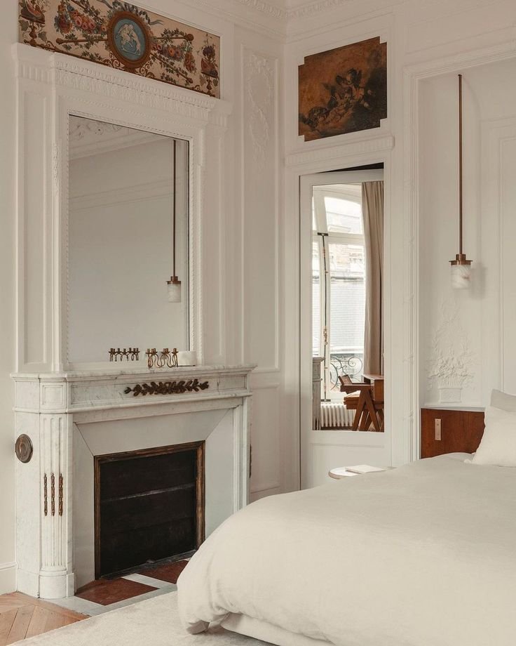 a white bedroom with a fireplace and mirror