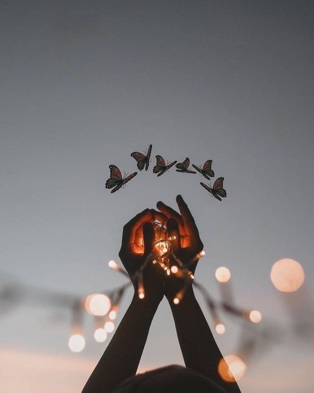 a person holding up their hands with butterflies flying in the air