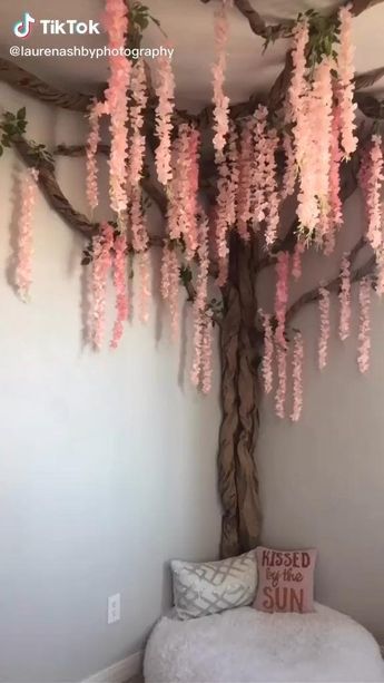 a tree with pink flowers hanging from it's branches in the corner of a room