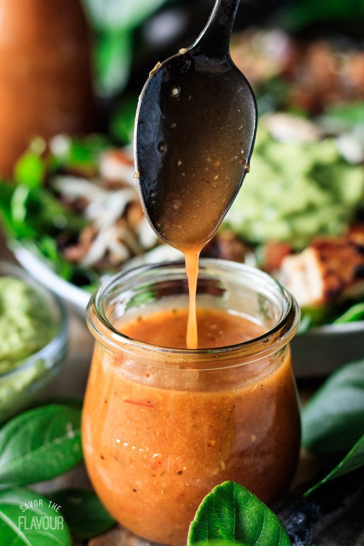 a spoon is pouring sauce into a jar