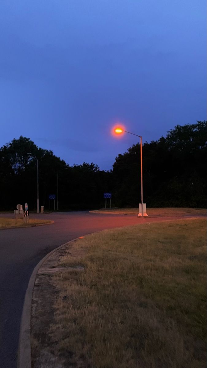 an empty street at dusk with people walking on the sidewalk and trees in the background