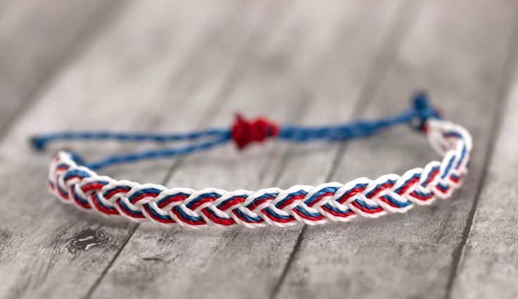 a red, white and blue braided bracelet sitting on top of a wooden table