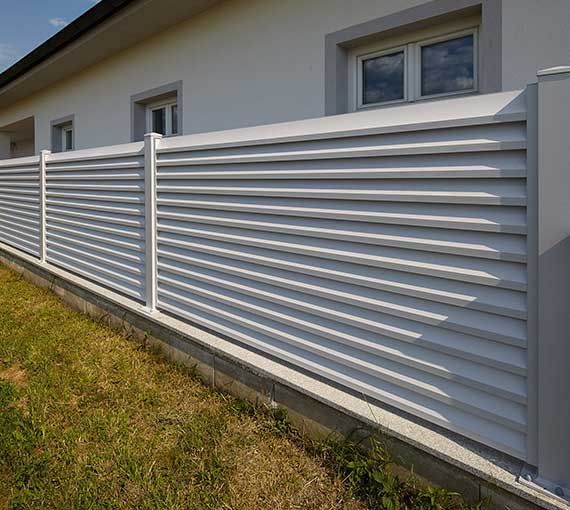 a white fence is in front of a house with grass on the ground and two windows