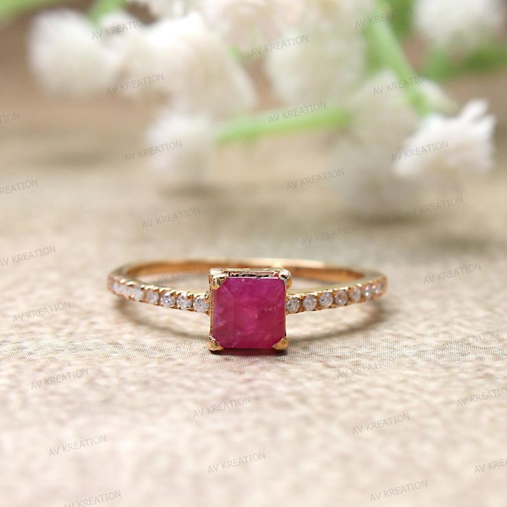 an engagement ring with a pink stone surrounded by white diamonds on a beige surface next to flowers